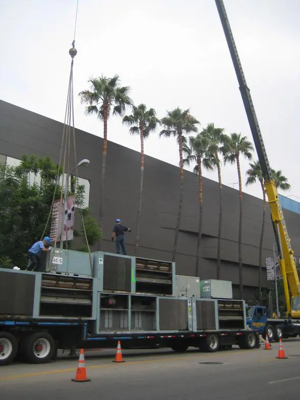 A crane is lifting a large box on the back of a truck.